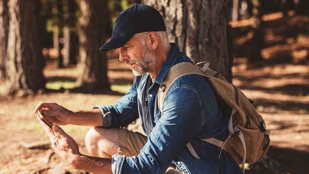 Un homme en randonnée dans les bois en faisant une pause pour vérifier son téléphone portable