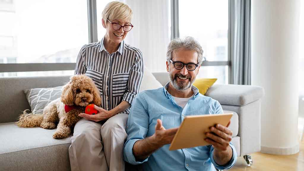 Un couple se détendant à la maison avec leur chiot golden doodle regardant quelque chose ensemble sur une tablette