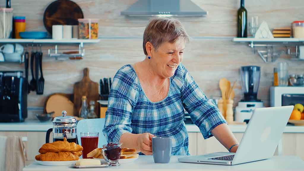 A woman standing at her kitchen island enjoying a cup of coffee as she works on her laptop