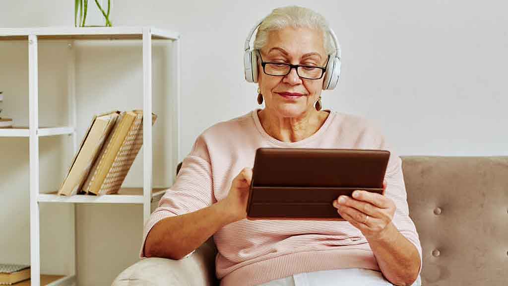 Une femme à la maison se détendant sur le canapé avec des écouteurs écoutant quelque chose sur une tablette